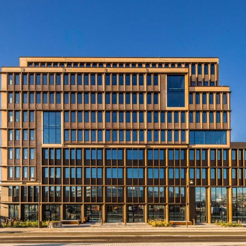 Moderne kontorbygning med store vinduer set udefra. I baggrunden ses en blå himmel.